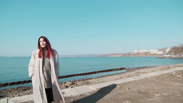 one girl in a coat stands on the shore of a calm sea