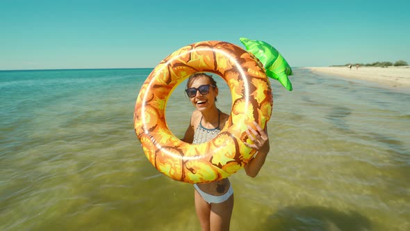 Portrait of Happy Smiling Young Woman in Sunglasses with Inflatable Pineapple Standing in Sea Water