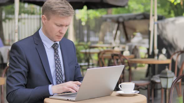 Businessman working on Laptop while Sitting in Outdoor Cafe