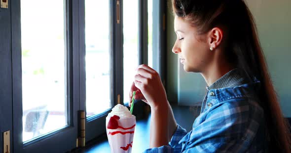 Happy woman looking through window while drinking milkshake