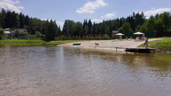 People Taking Rest at the Beach Area with Sand and Loungers Near a Small Lake in a Cottage Village