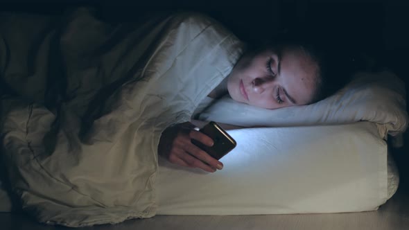 Woman lying in bed, falls asleep putting and turn off  smartphone.