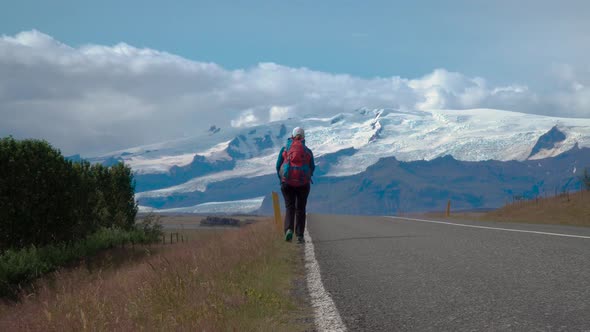 Woman Traveler with a Backpack Is on an Asphalt Road