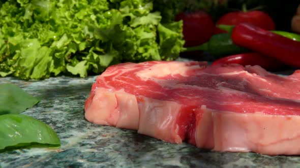 Closeup of the Raw Steak Falling on Stone Table on the Background of Vegetables