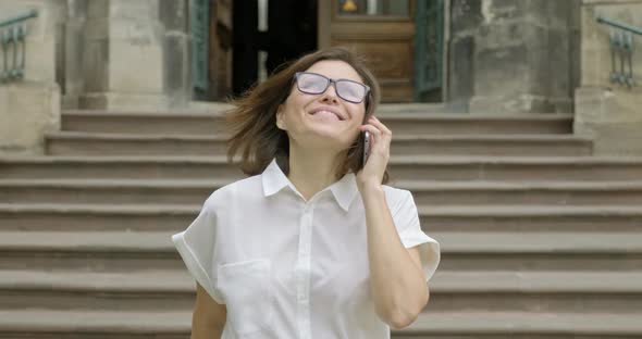 Mature Smiling Positive Woman in Glasses Light Blouse Walking on the Stairs Talking on the Phone