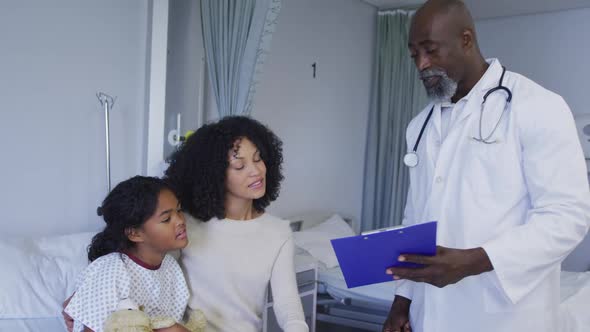 African american senior male doctor with clipboard talking to mother and daughter at hospital