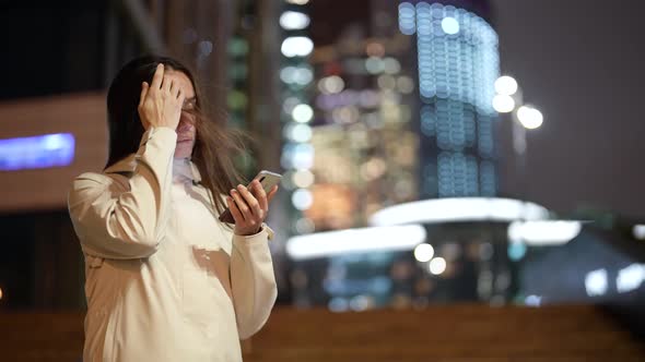 Brunette Woman is Chatting Online in Social Networking By Smartphone Standing on Street in Evening