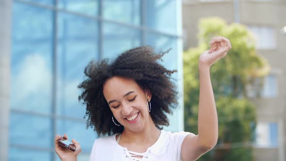 Happy Laughing White-toothed African American Girl Model Jumps High and Rejoices with Smartphone in