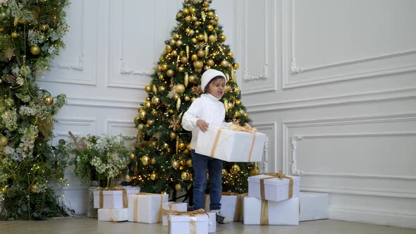 Boy Child in a White Sweater and Hat Stands at the Christmas Tree