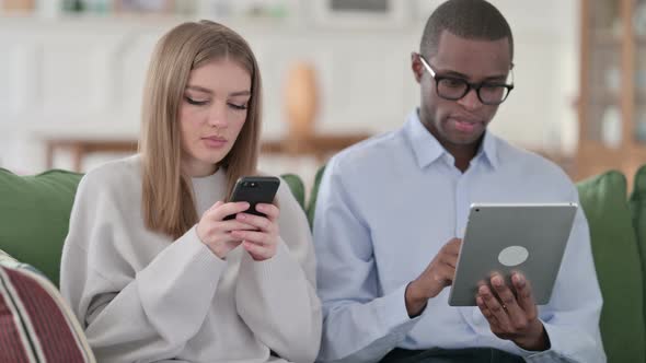 Woman Using Smartphone While Man Using Tablet at Home Couple