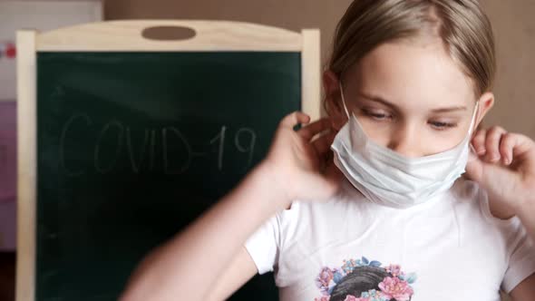 A Little Girl at Home Wears a Medical Mask Behind the Inscription COVID19