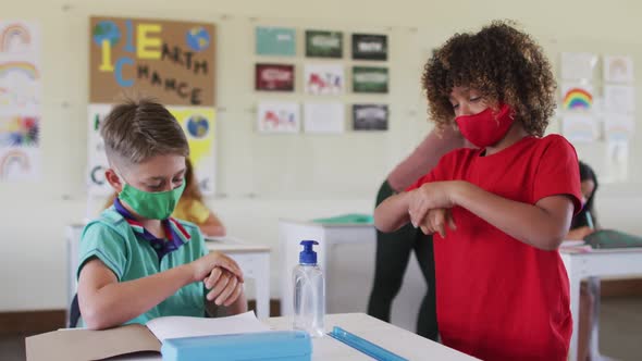 Two boys wearing face masks sanitizing their hands in class at school