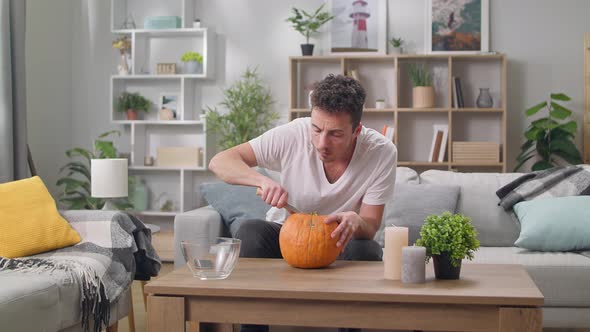 Young Man Carves Jack Lantern with a Knife in Living Room