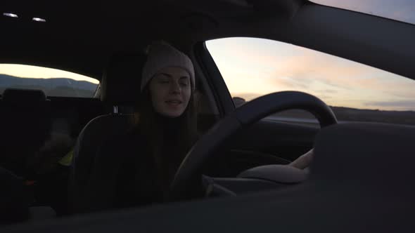 Front View of Woman in Winter Clothes Driving Car and Choosing Song on the Radio