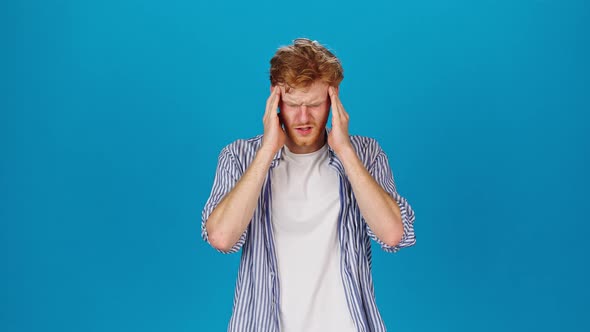 Redhead Man Suffers From Headache on Blue Background