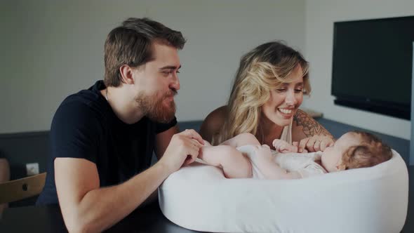 Bearded Handsome Smiling Dad Kissing Leg or Feet of His Newborn Child While Mother Communicate with