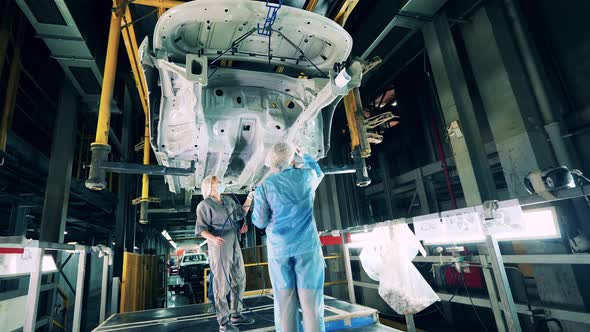 Car Factory Workers Painting a Vehicle Body From Below at a Car Factory