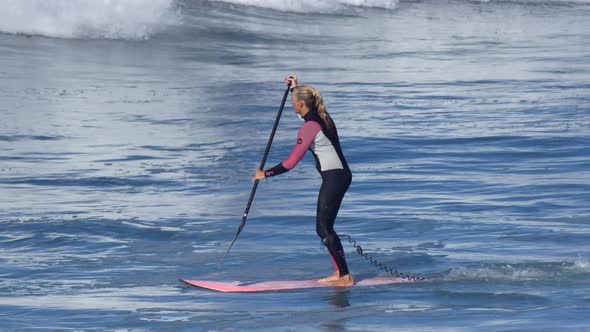 A woman rides an sup stand up paddleboard while surfing on a pink surfboard