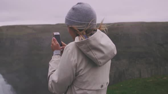 Young Woman Touristtaking Pucture with Smartphone of Waterfall in Iceland Gimbal Shot Slow Motion