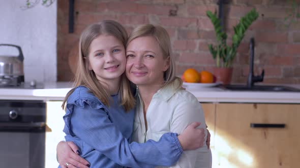 Love Mother, Portrait of Happy Mom with Little Daughter Embracing and Kisses on Cheek in Kitchen at