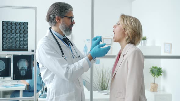 Side View of Female Patient Opening Mouth Showing Sore Throat to Doctor in White Gown in Hospital