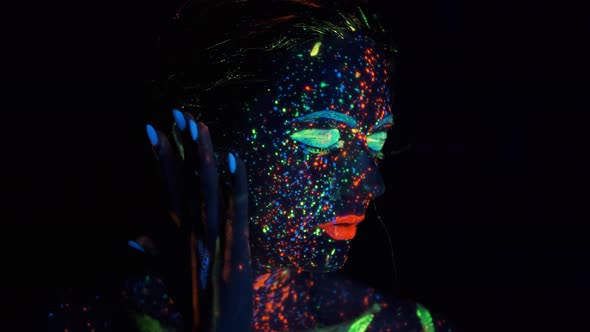 Closeup Face of Beautiful Brunete Woman in Neon Light. Face Painted with Glow in the Dark Paint