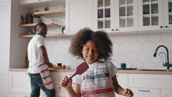 Close Up Portrait of Cute Little African American Girl Singing with Cooking Spatula at Kitchen