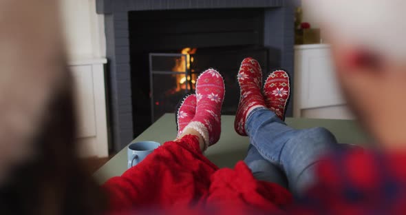 Feet of caucasian couple sitting on sofa, wearing christmas socks and santa hats