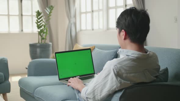Male Working On Laptop With Green Screen Mock Up Display At Home Living Room While Lying On A Sofa