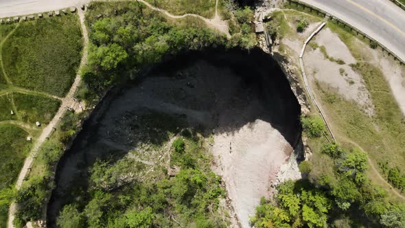 Descending aerial top down shot of gigantic hole with ribbon waterfall on Niagara Escarpment, in the