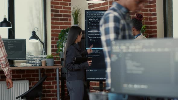 Software Engineer Holding Digital Tablet Analyzing Code on Wall Screen Tv Explaining Errors to
