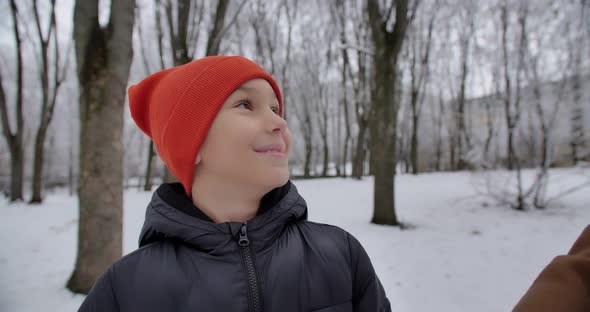 In A Snowy Park, A Boy And His Mother Hold Hands And Talk Happily