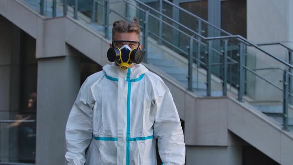 Portrait of a Young Man in a Protective Suit, Respirator and Gloves Looks Into the Camera, Puts on