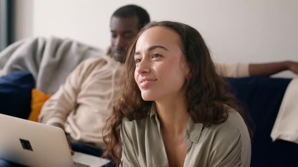 Portrait Of Relaxed Young Couple At Home Sitting On Sofa Browsing Internet On Laptop Computer