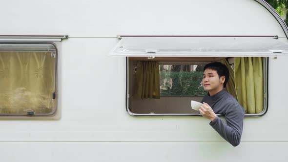 happy young man drinking coffee at window of a camper RV van motorhome