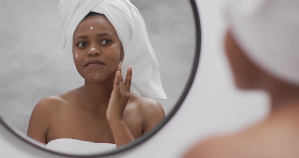 Happy african american woman apply cream on face in bathroom