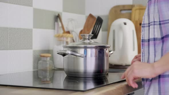 Woman's Hands with Saucepan on Cooking Glass Ceramic Surface Female Turning on Stove