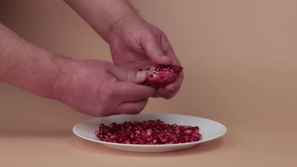 Closeup Male Hands Peel Grains From a Wedge of Red Pomegranate on a White Plate