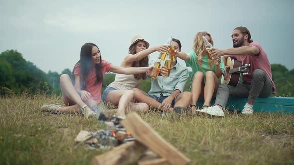 Happy Friends Drinking Beer, Having Fun And Sitting Near Bonfire