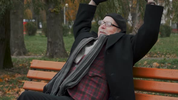 Serene attractive elderly senior resting on bench taking deep breath of fresh air holding hands behi