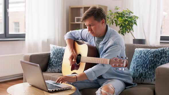 Young Man with Laptop Playing Guitar at Home