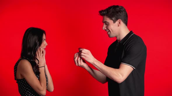 Young Couple. Man Makes Marriage Proposal To His Lover Woman with Ring on Red