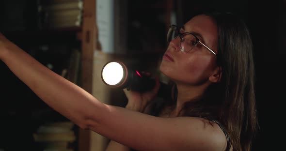 Girl with Lantern Views Library Shelves in Darkness is Shocked Pulls Out Book