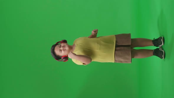 Full Body Of Asian Little Boy Listening To Music With Headphones And Dancing In The Green Screen