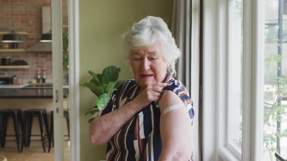 Happy caucasian senior woman showing plaster on arm after covid vaccination