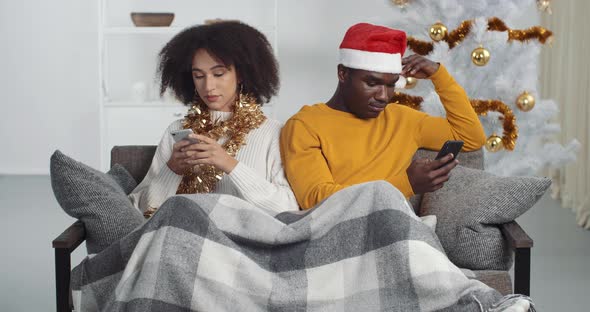 Afro American Couple Sitting on Sofa in Christmas Looking in Different Directions Use Phones Mobile