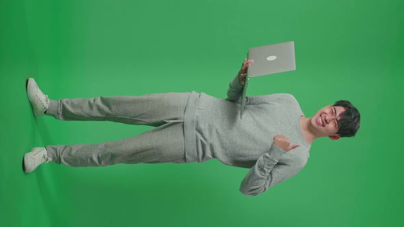 Full Body Of Smiling Asian Man Showing Thumbs Up Gesture While Typing On Computer On Green Screen