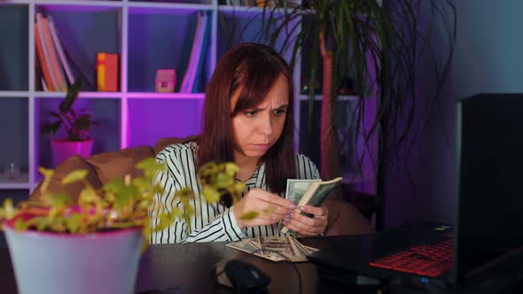 Thoughtful Woman Counts Money Sitting in Armchair Before Computer in Office