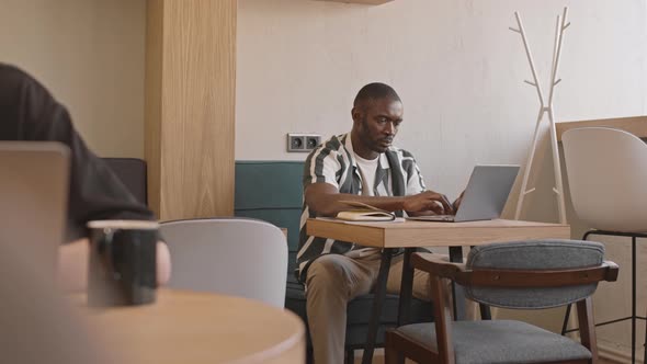 African-American Male Freelancer Working on Laptop in Cafe