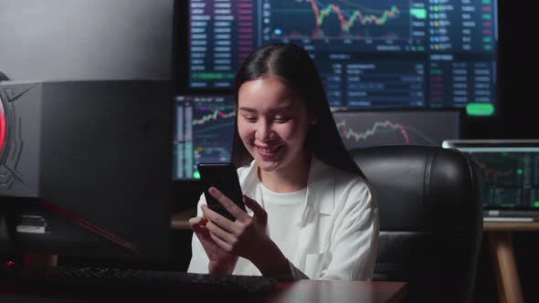 Female  Stock Market Broker Using Mobile Phone With Analyzing Graphs On Multiple Computer Screens